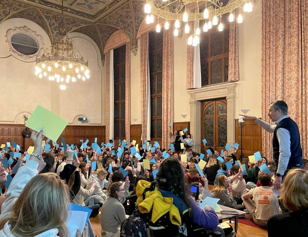 Interactive leadership workshop with large audience holding blue and yellow voting cards during a team collaboration exercise